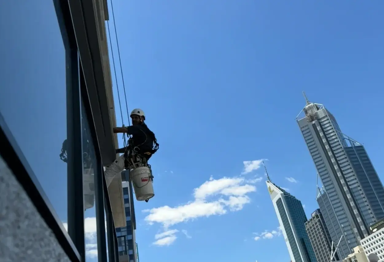 High rise window cleaner on rope access cleaning glass with the Perth CBD skyline behind